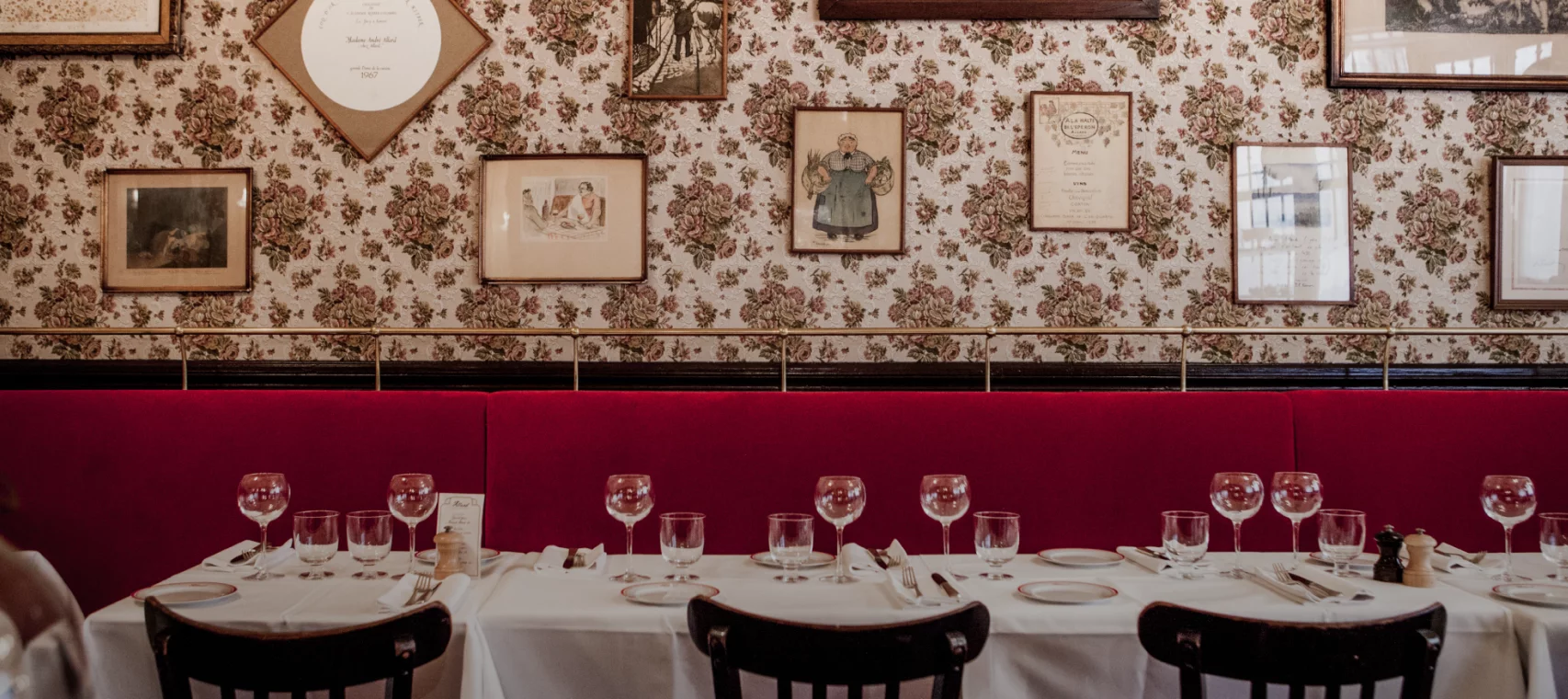 Classic Parisian bistro interior with red banquette, white linens, and framed art on floral wallpaper
